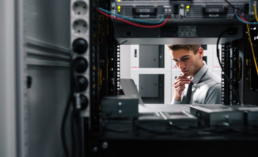 IT professional inspecting a server rack, looking at a laptop in a data center.