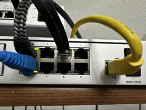 Network switch with blue and yellow Ethernet cables plugged into ports, showing port numbers and cables in use.