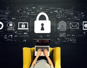 Person typing on a laptop on a yellow chair, with large padlock and digital security icons floating above, illustrating cybersecurity.