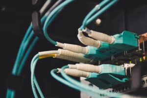 Close-up of teal Ethernet cables plugged into a network patch panel in a server rack, dimly lit.