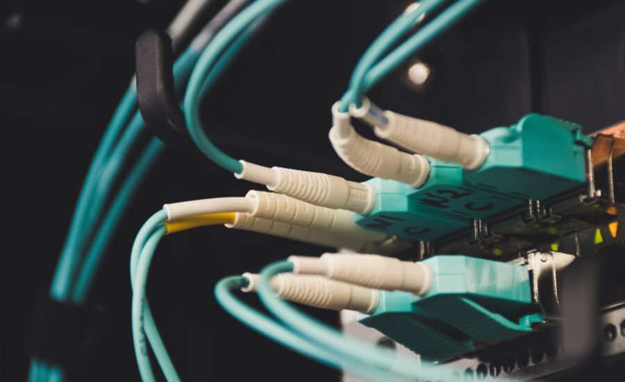 Close-up of teal Ethernet cables plugged into a network patch panel in a server rack, dimly lit.
