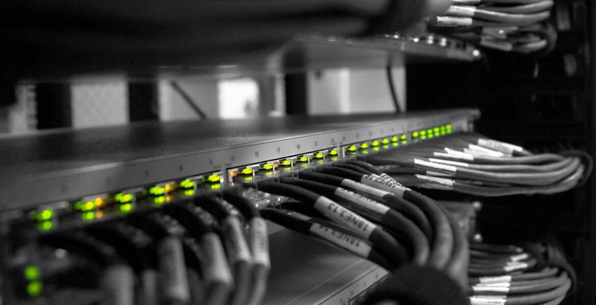 Network rack with a row of illuminated green LEDs on a switch and bundled Ethernet cables labeled and organized in a server cabinet