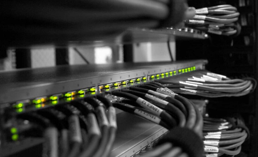 Network rack with a row of illuminated green LEDs on a switch and bundled Ethernet cables labeled and organized in a server cabinet