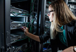 Female IT technician in a data center plugs a network cable into a rack-mounted server.