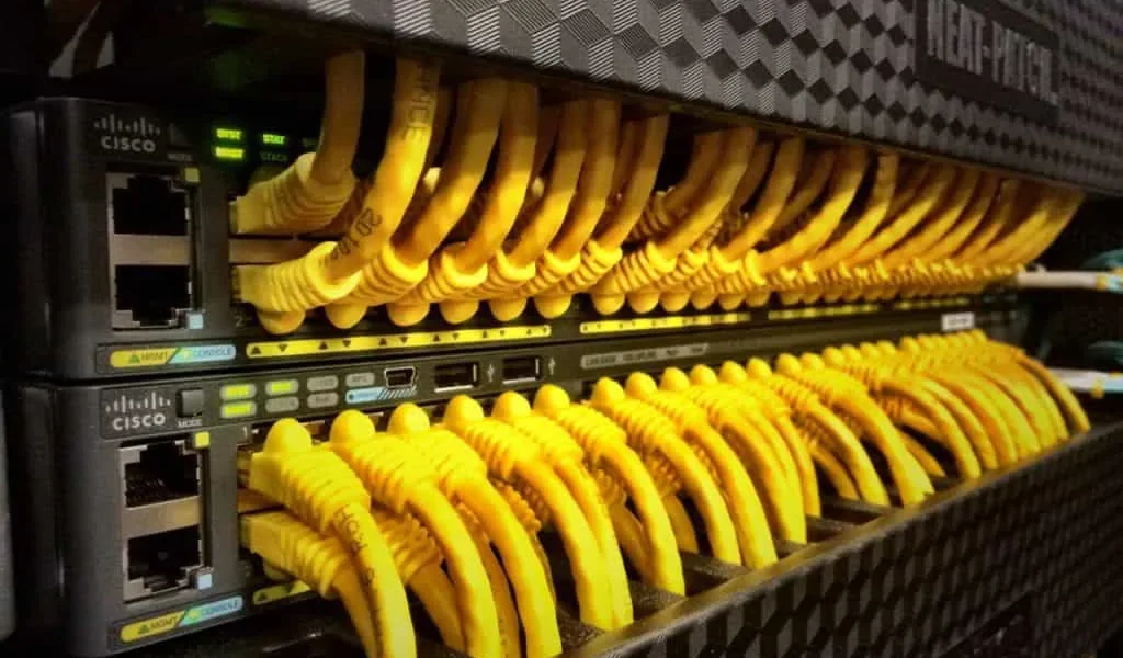 Row of Cisco network switches with numerous yellow Ethernet cables connected.