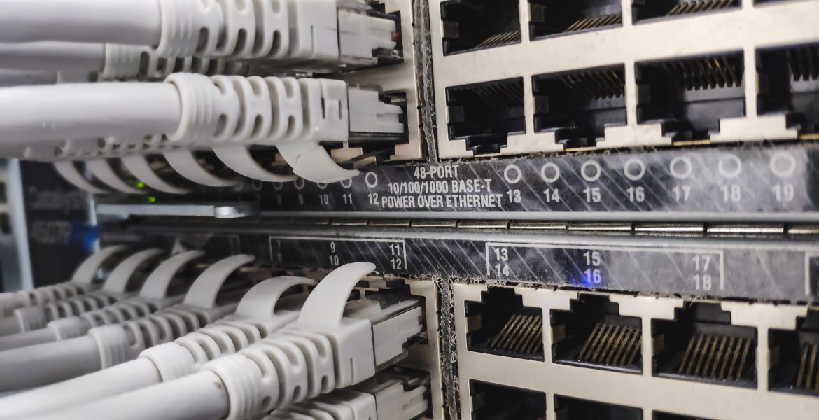 Close-up of a network patch panel with multiple RJ-45 Ethernet ports and gray cables plugged into them in a server rack, showing data cabling.